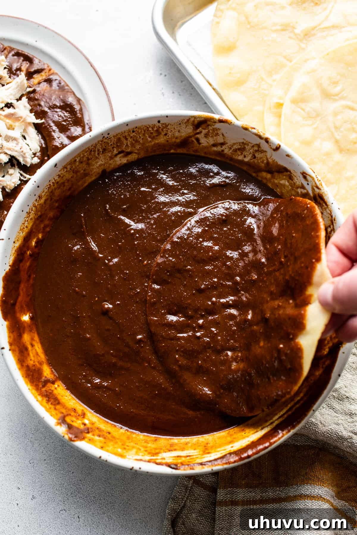 Mexican Mole Bliss 6 A golden, lightly fried corn tortilla is elegantly submerged into a pan brimming with rich, dark mole sauce, ensuring every inch is coated for maximum flavor.