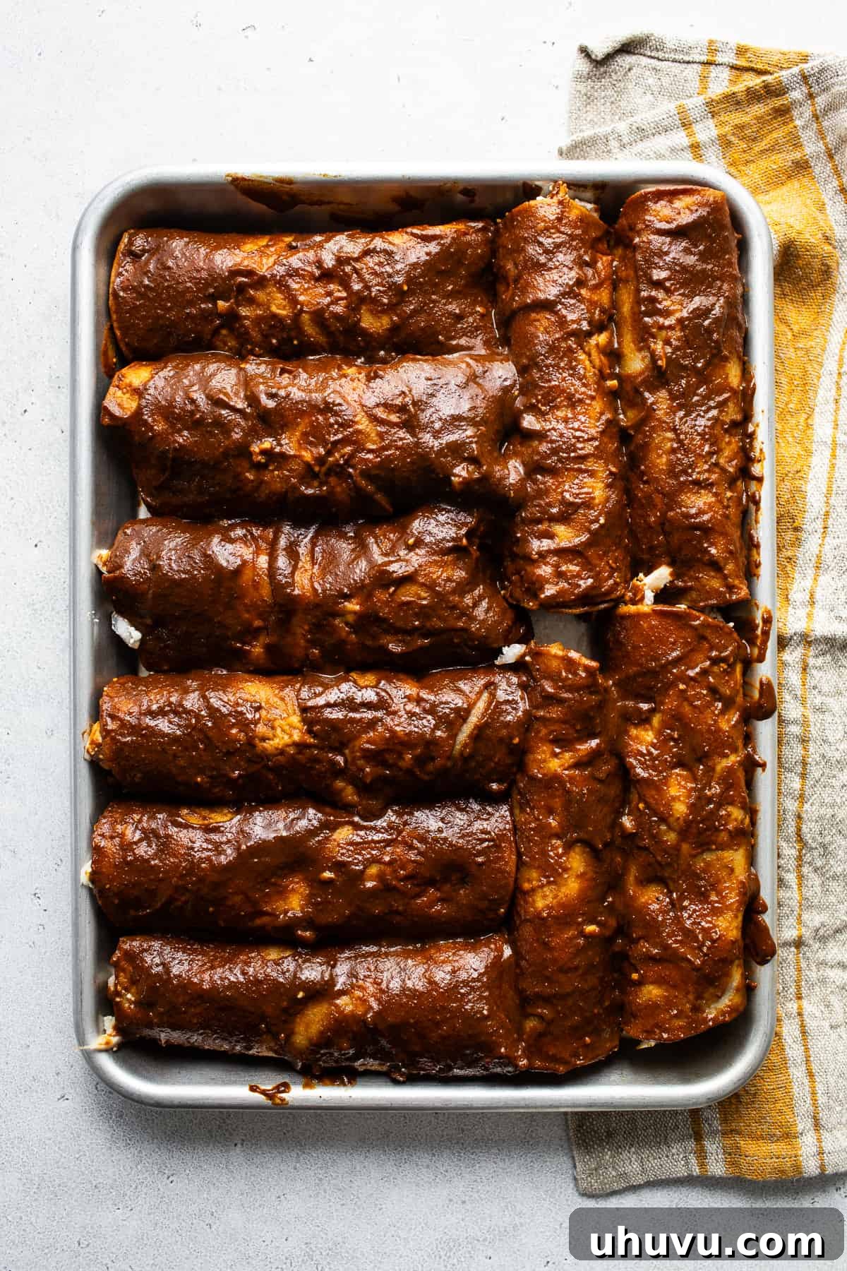 Mexican Mole Bliss 7 A row of perfectly filled and rolled enmoladas neatly arranged on a baking sheet, glistening with mole sauce, poised for their final garnishes before serving.