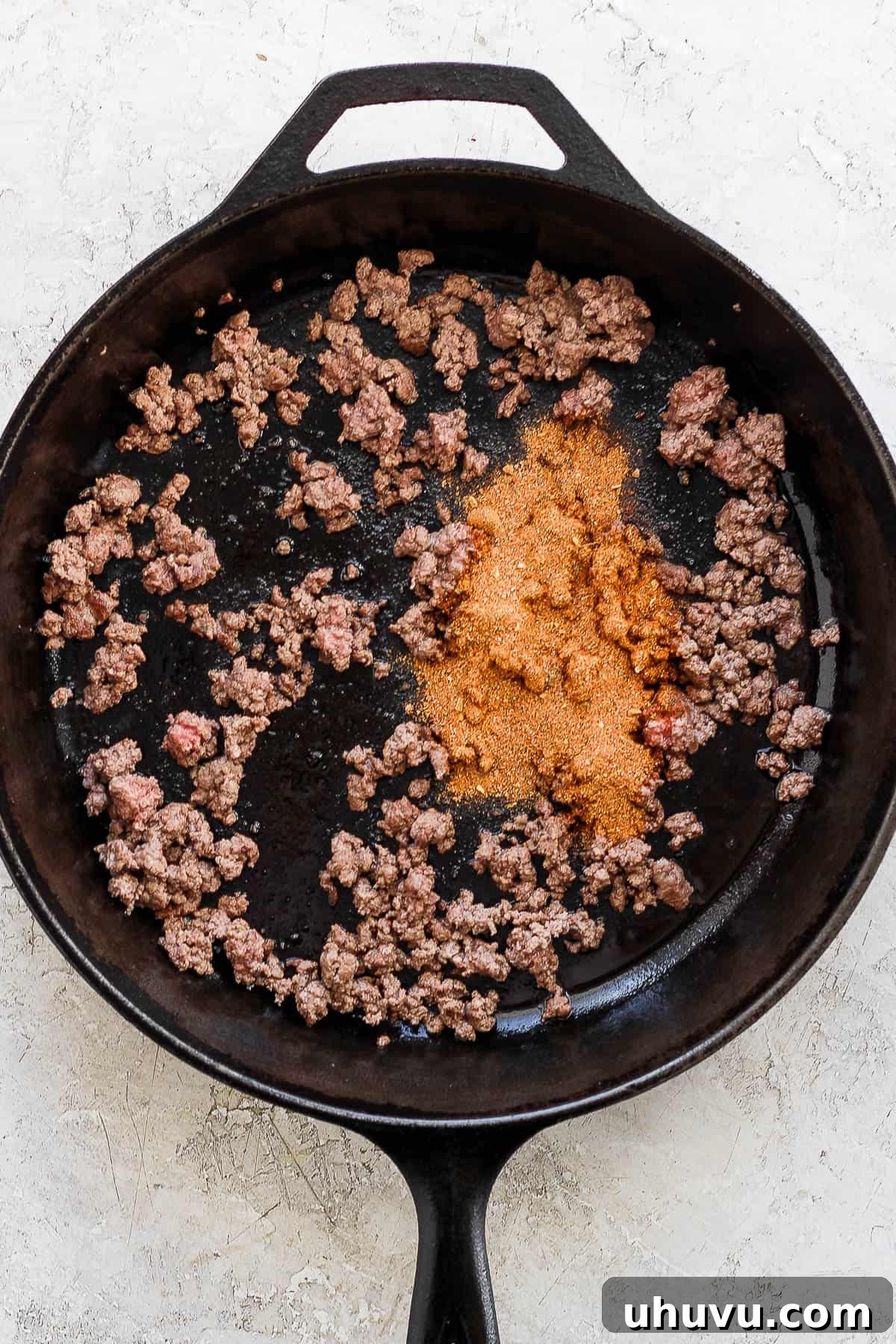 Zesty Mexican Pizza 4 Ground beef cooking in a cast iron skillet with taco seasoning being added.