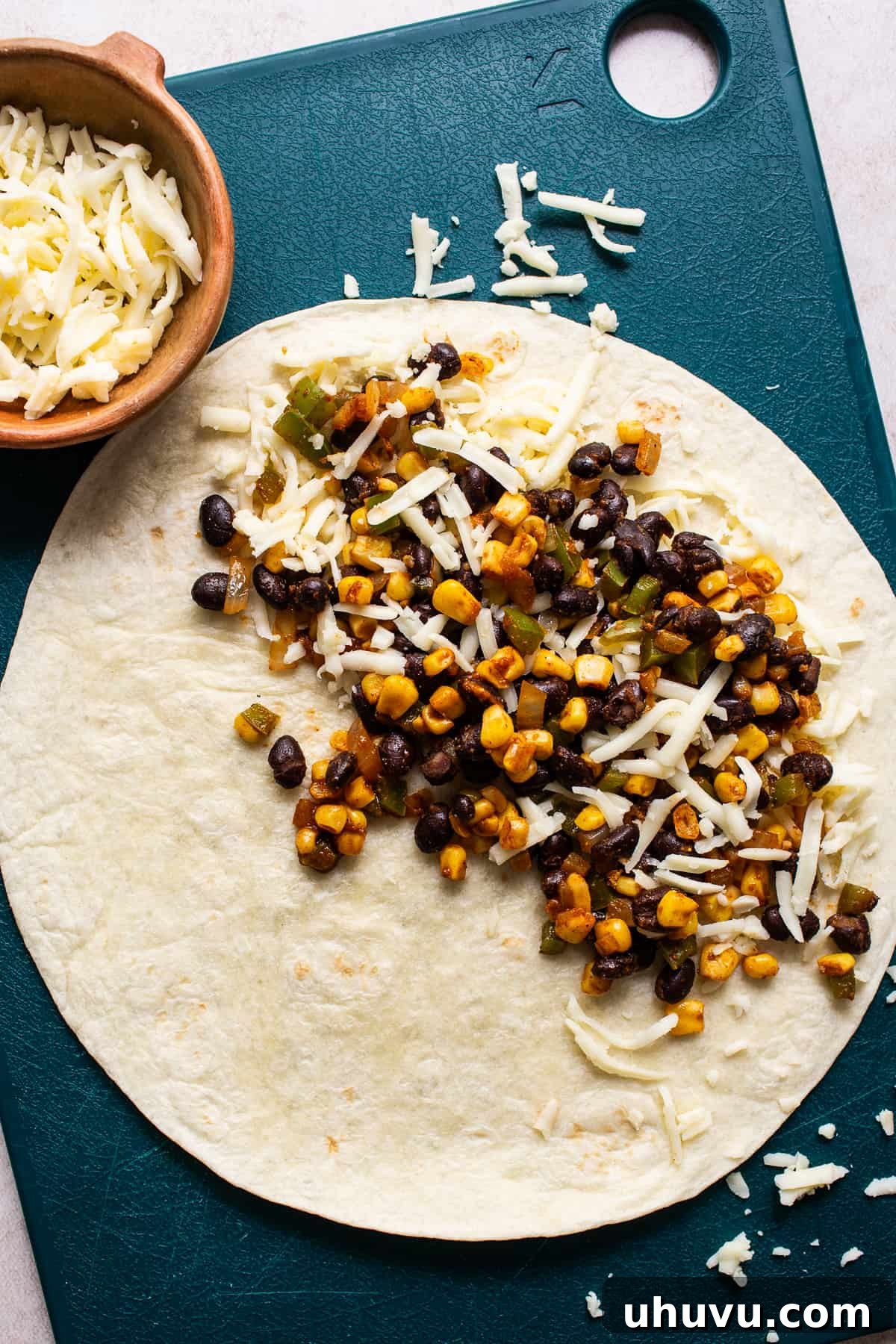 Fiesta Black Bean Melts 6 A black bean quesadilla being assembled on a cutting board with shredded cheese.