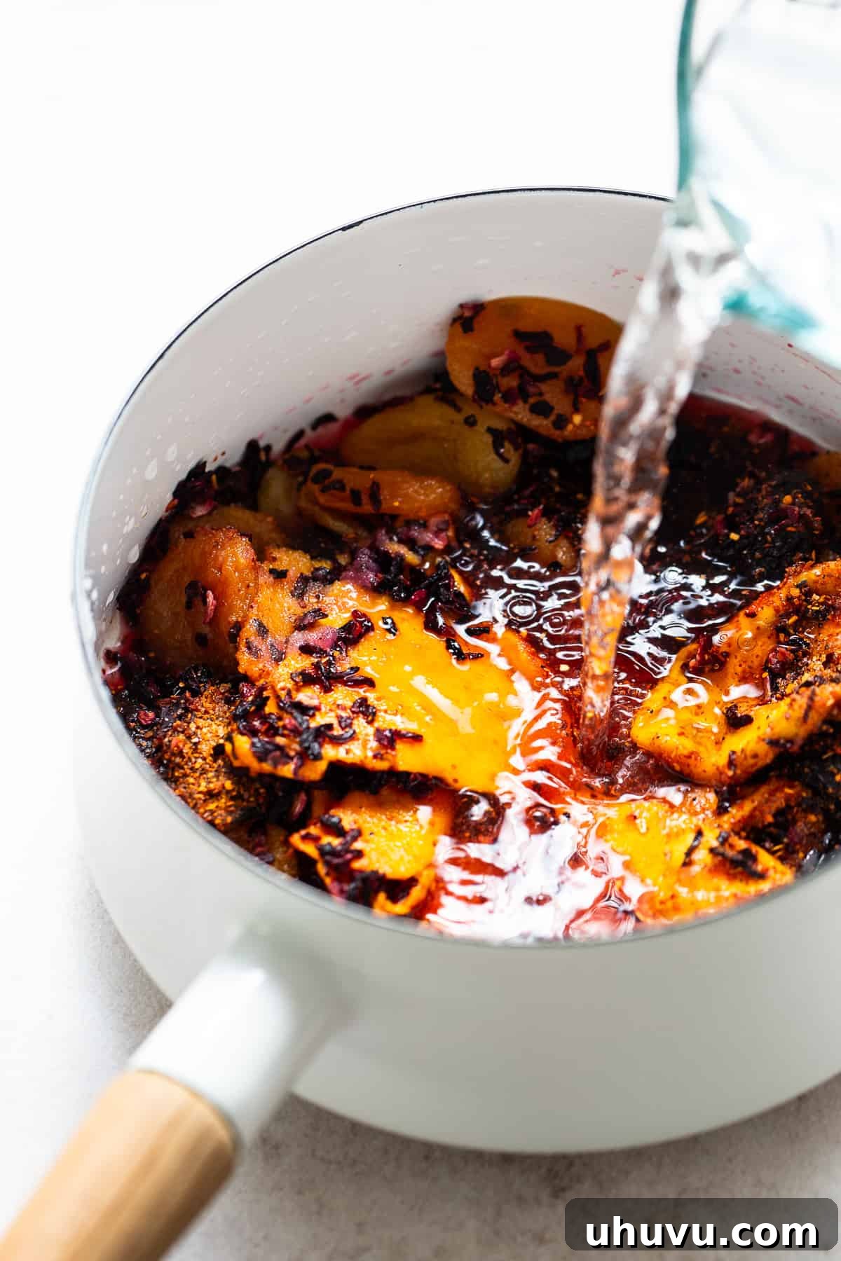 Homemade Chamoy Perfection 4 Water being poured into a pot of ingredients, including various dried fruits, hibiscus, and spices, as part of the homemade chamoy preparation process.