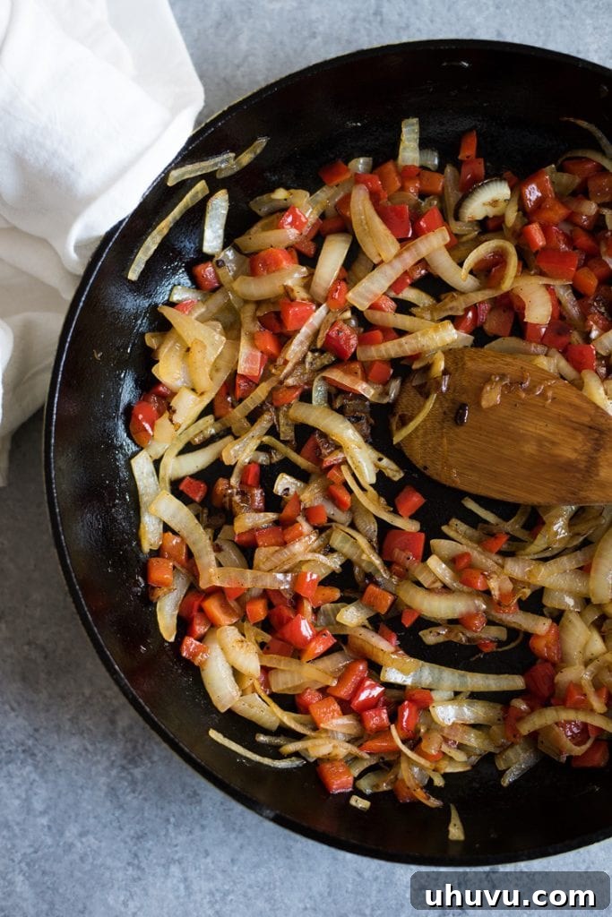 A close-up shot showing the initial steps of how to make shakshuka, with finely sliced onions and peppers caramelizing in a hot skillet, laying the foundation for rich flavor.