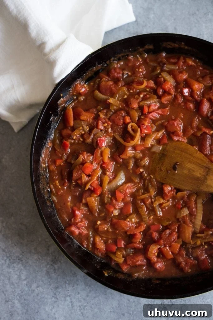 A vibrant red shakshuka sauce simmering to perfection in a cast iron pan, showing the rich texture and color of the tomato and spice base before the eggs are added.