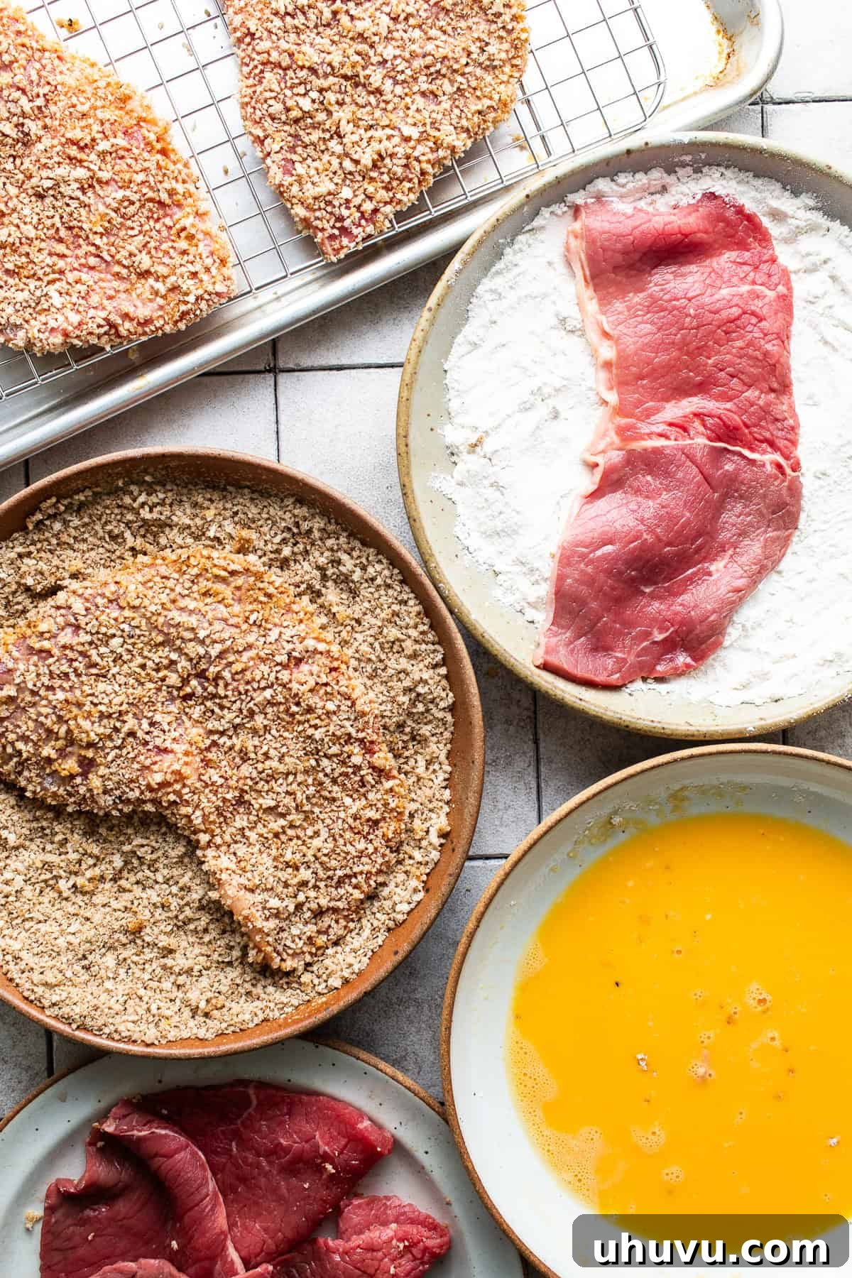 A milanesa cutlet being breaded in a bowl, coated in panko breadcrumbs and seasonings.