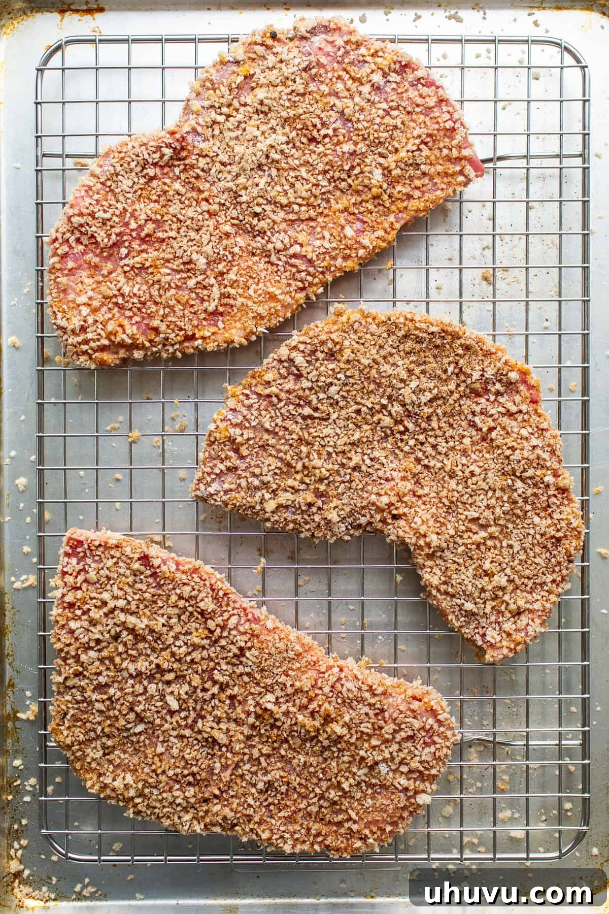 Breaded Torta de Milanesa cutlets neatly arranged on a sheet pan, ready to be fried.