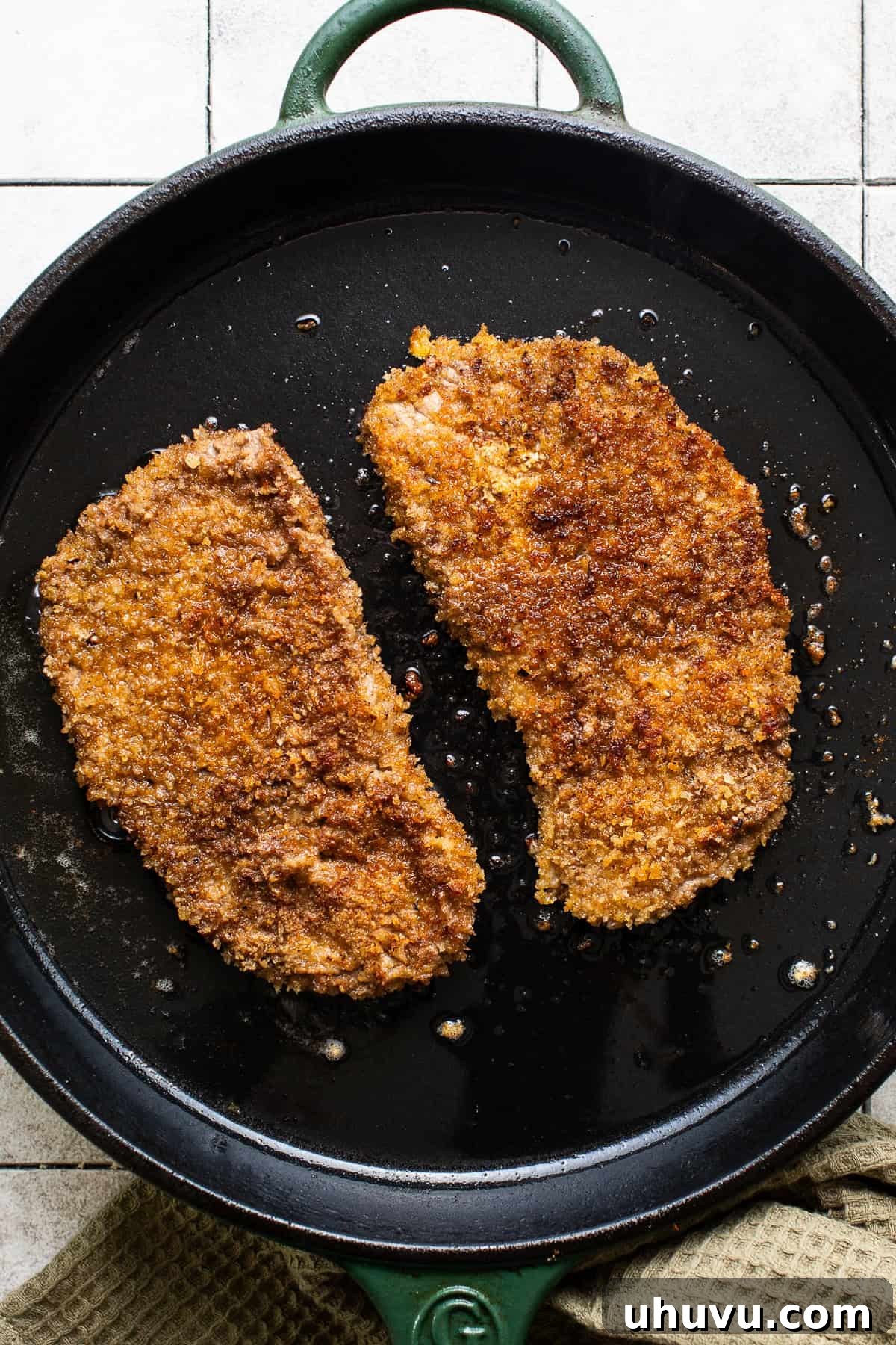 A close-up of a golden-brown, crispy milanesa fresh out of the frying pan, resting on paper towels to absorb excess oil.