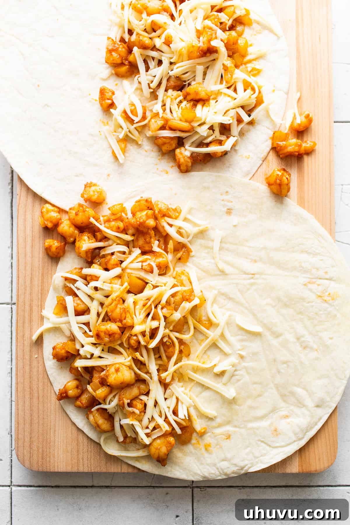 Zesty Shrimp Queso Melts 6 Two open flour tortillas on a skillet, each with a generous layer of cooked shrimp, onions, bell peppers, and shredded Mexican cheese on one half, ready to be folded.