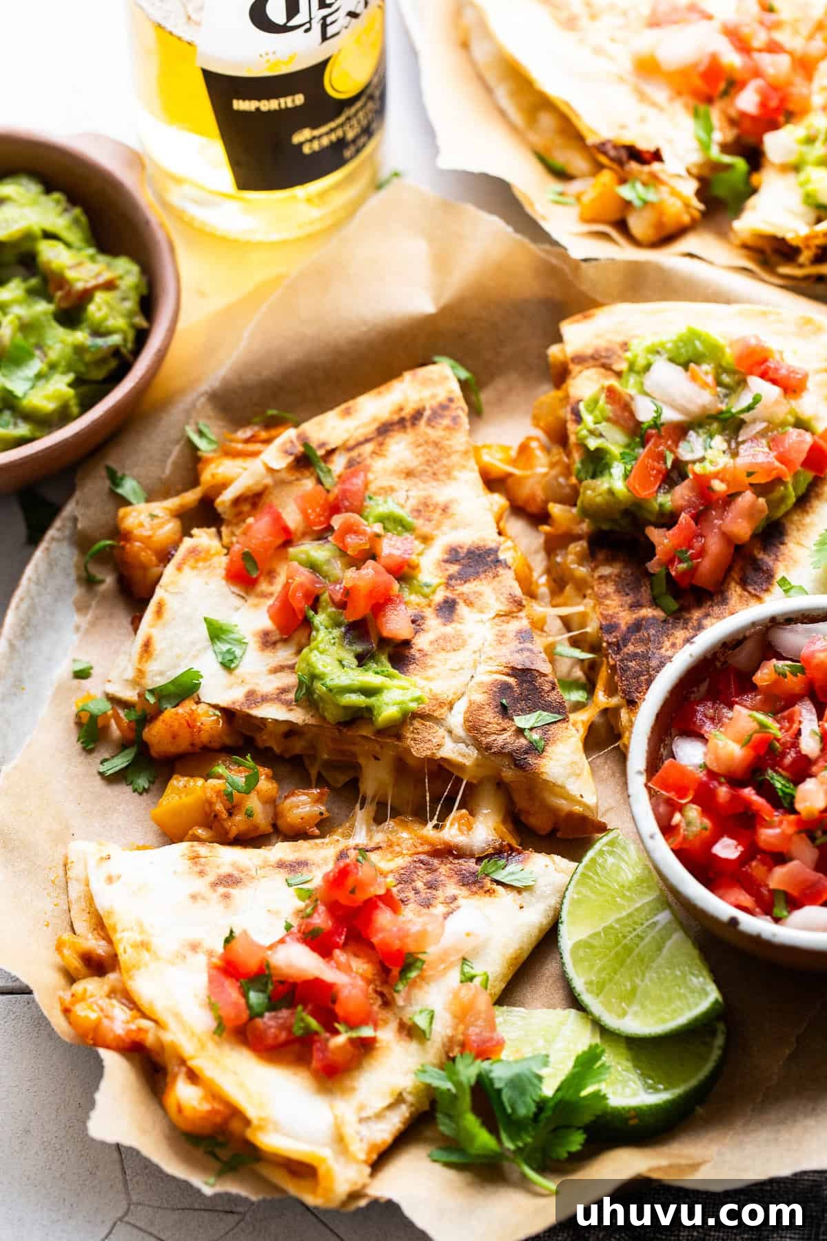 Zesty Shrimp Queso Melts 7 Three perfectly cooked shrimp quesadillas stacked on a plate, surrounded by a bowl of fresh pico de gallo and a side of creamy guacamole, ready to be enjoyed.