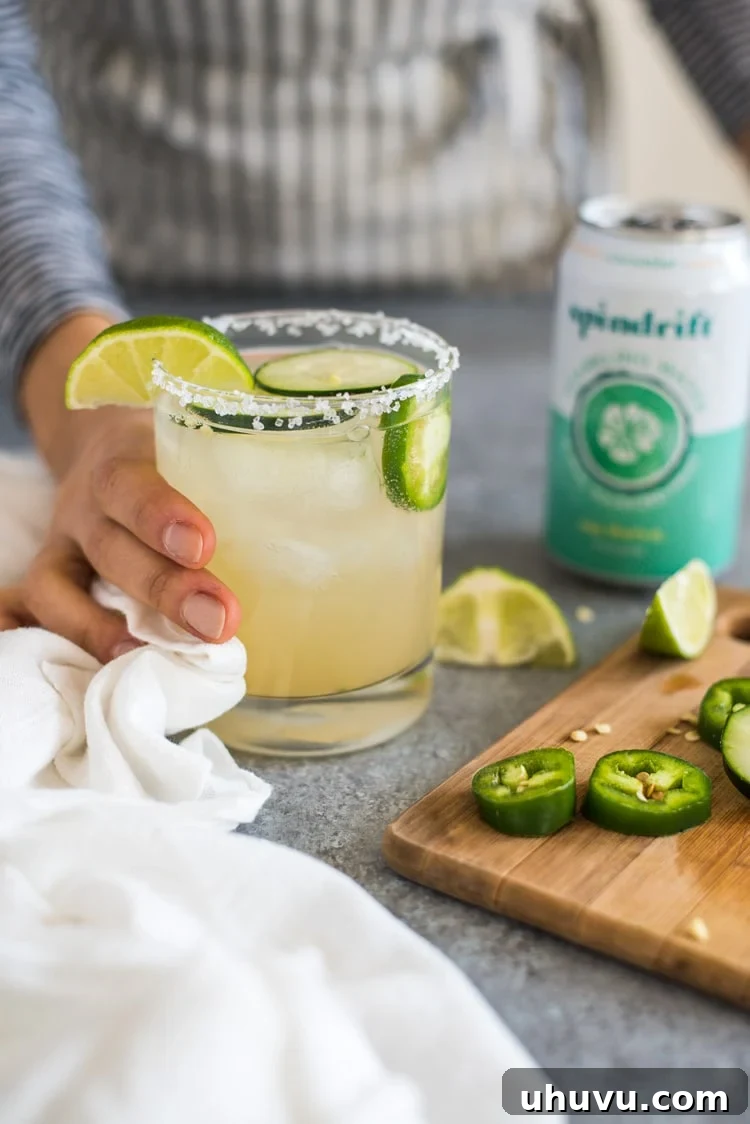 Cool Heat Margarita 2 A vibrant Cucumber Jalapeño Margarita cocktail, garnished with cucumber slices and jalapeño rounds, sitting on a rustic surface. Perfect for a refreshing and spicy drink experience.