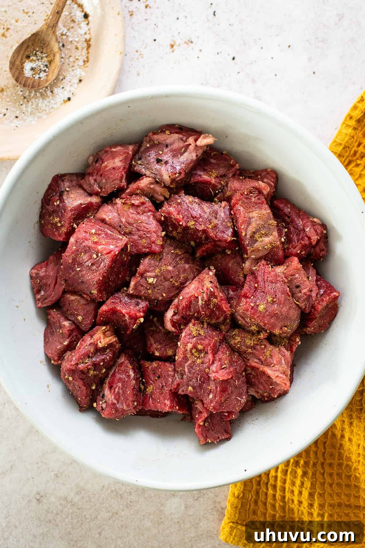 Slow-Simmered Beef Perfection 4 Diced sirloin steak seasoned generously with kosher salt, ground cumin, Mexican oregano, and black pepper in a large bowl, ready for searing.