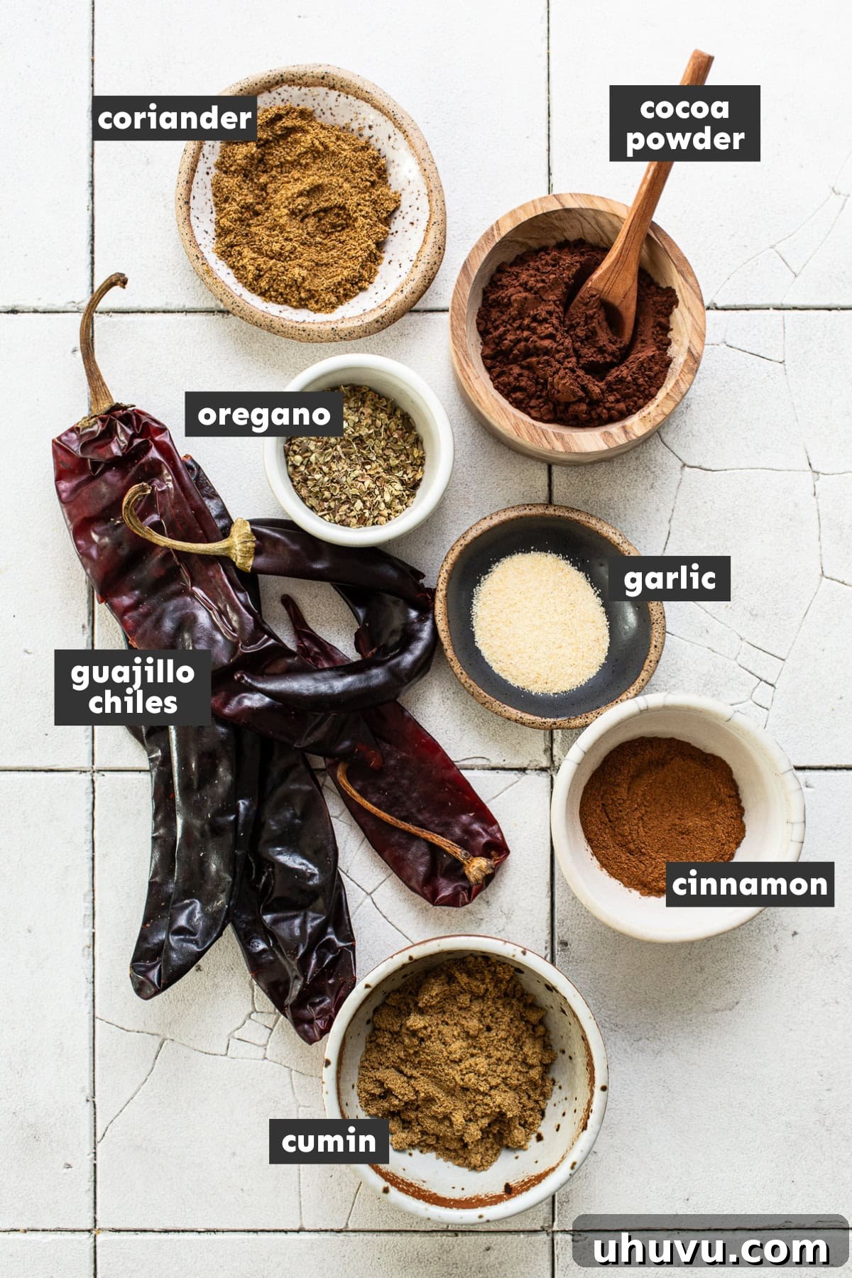 Your Signature Chili Powder Blend 3 A selection of ingredients for homemade chili powder laid out on a table, including dried guajillo chiles, various ground spices, and cocoa powder.