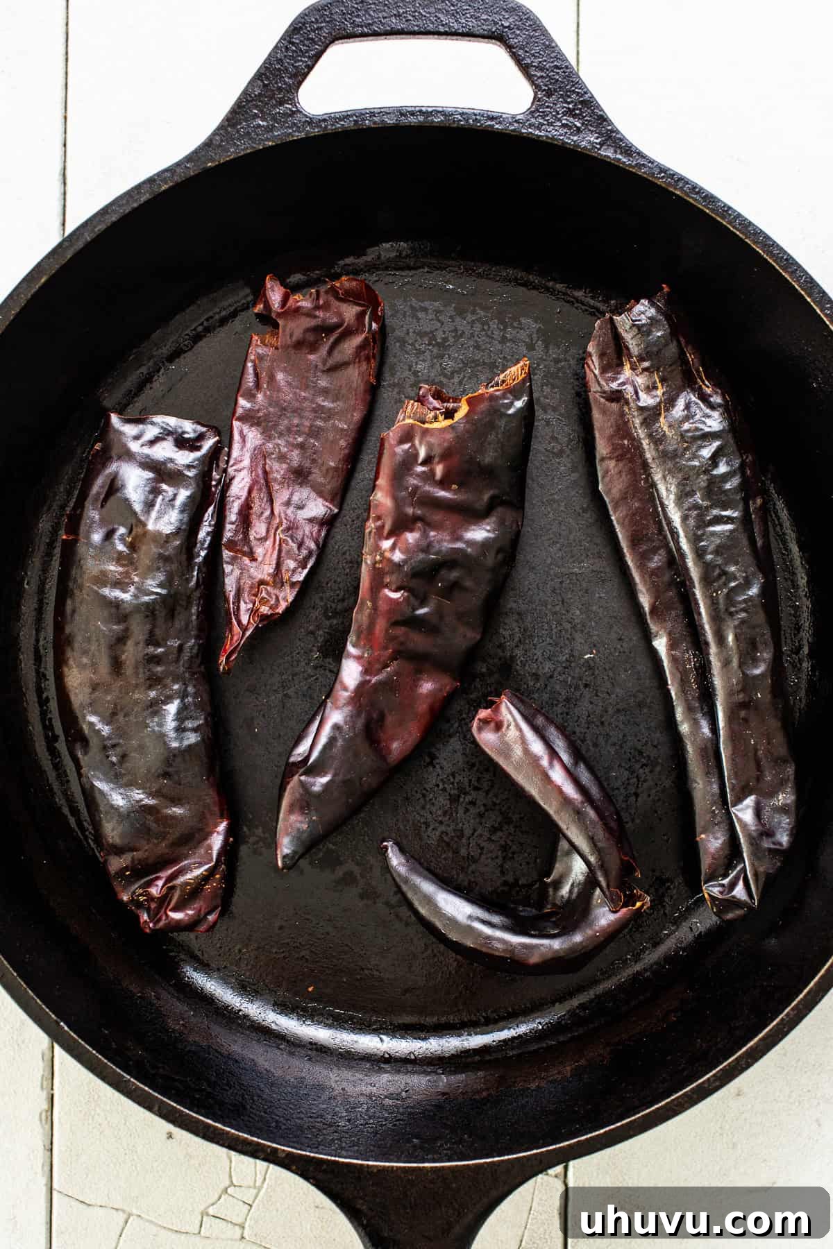 Your Signature Chili Powder Blend 4 Dried guajillo chiles being toasted in a cast iron skillet over medium-high heat.