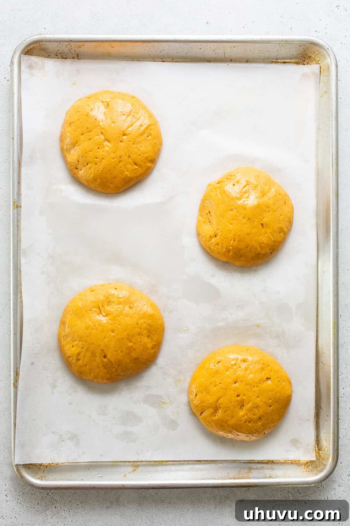 Spiced Pumpkin Conchas 4 Four round balls of pumpkin concha dough resting and rising on a parchment-lined baking sheet.