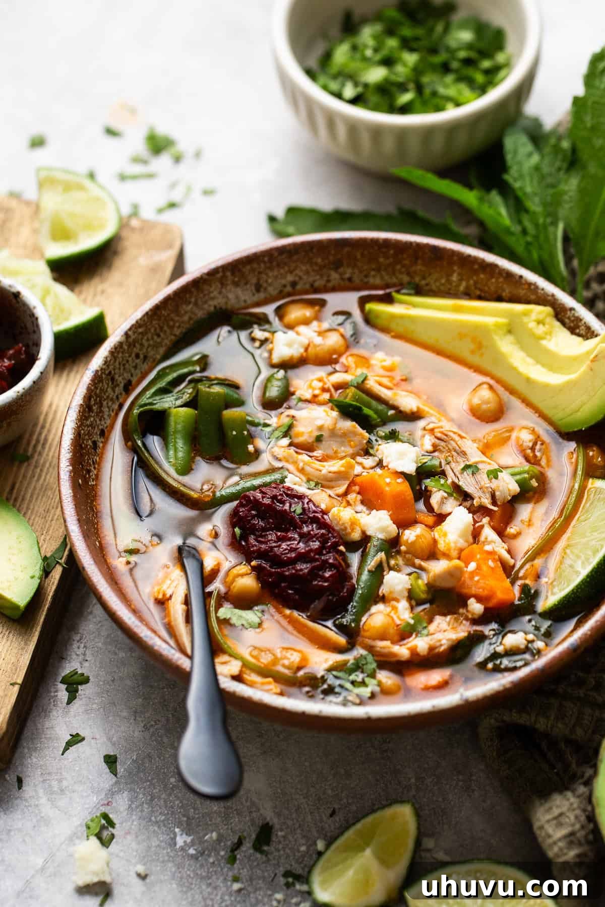 A beautifully presented bowl of Caldo Tlalpeño, garnished with fresh lime wedges and cilantro, sitting on a rustic wooden table, inviting diners to enjoy its warmth and flavor.
