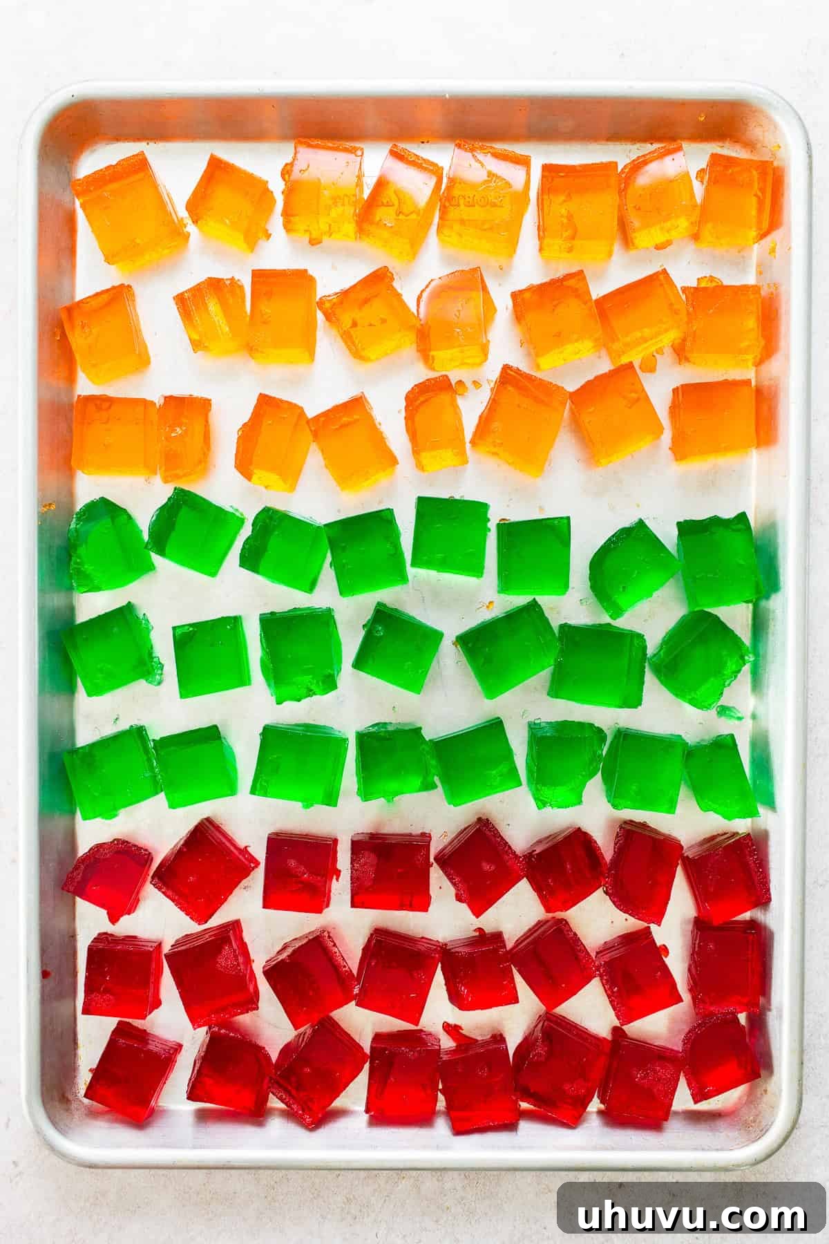 Mosaic Gelatin 5 Orange, green, and red cubes of jello neatly sliced into squares and arranged on a baking sheet, ready to be incorporated into the Gelatina de Mosaico.
