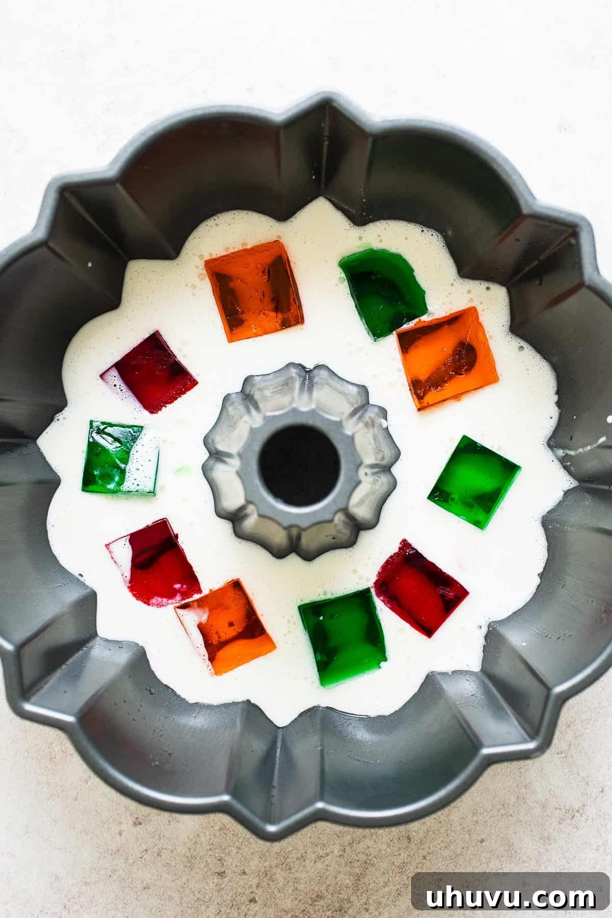 Mosaic Gelatin 7 A bundt pan being filled with layers of white milk gelatina and colorful cubes of flavored jello during the assembly of Gelatina de Mosaico.