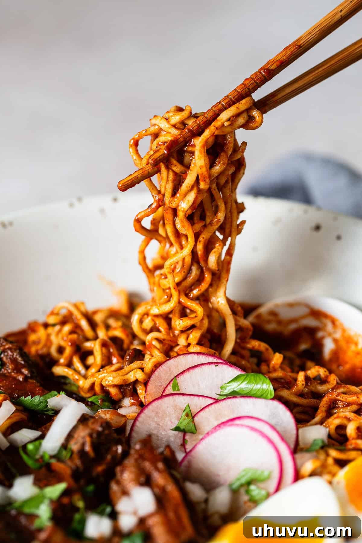 Ultimate Birria Ramen 6 A close-up shot of Birria Ramen, with chopsticks pulling up a generous tangle of noodles, revealing the rich broth and tender meat, ready for a satisfying slurp.