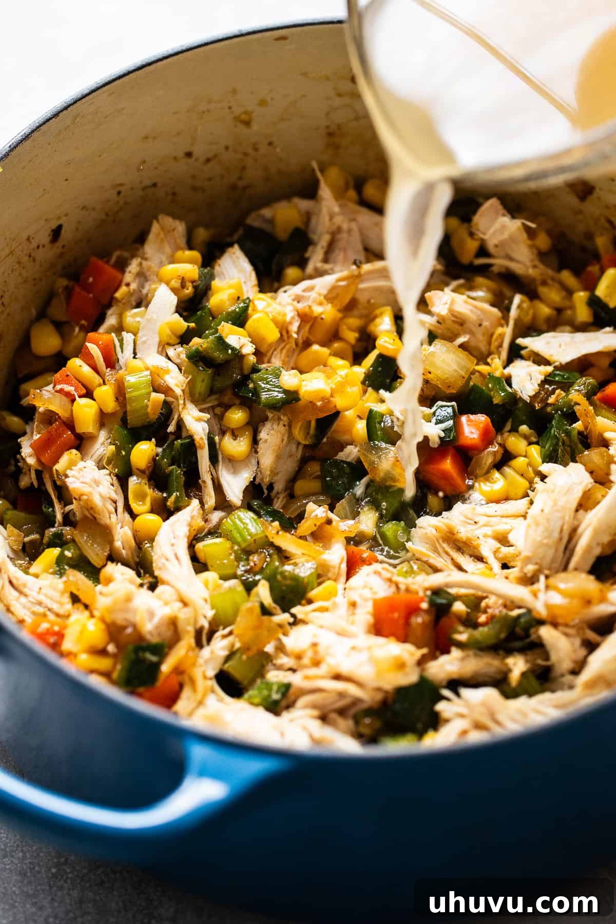 Smoky Chicken Poblano Soup 5 Chicken broth being poured into a pot with shredded chicken and corn.