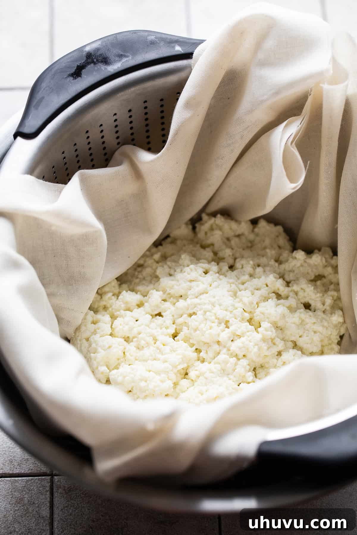 Make Your Own Queso Fresco 5 A colander lined with cheesecloth holds fresh cheese curds, draining excess whey into a bowl below.