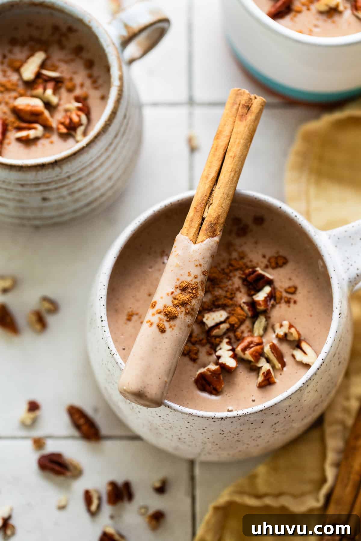 Cozy Walnut Brew 8 A single mug of hot atole de nuez, garnished with a cinnamon stick and a sprinkle of chopped pecans, sitting on a wooden surface.