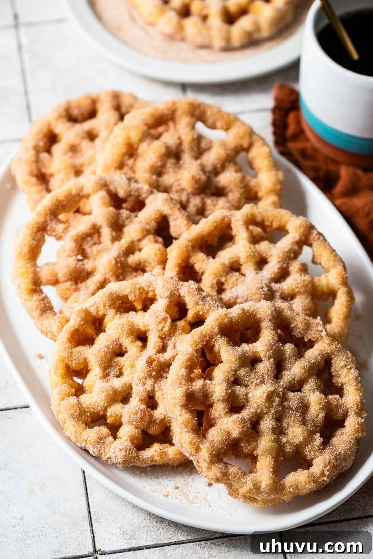Wind Fritters 9 Freshly made buñuelos de viento served on a large serving tray, beautifully coated in a cinnamon sugar mixture and ready to be enjoyed.