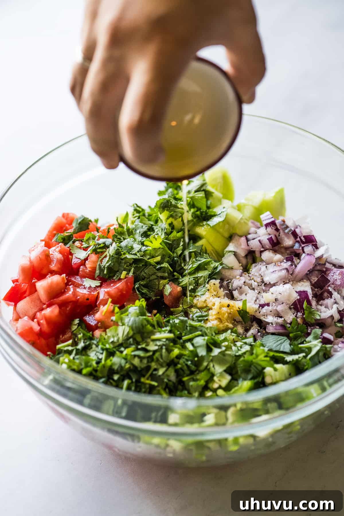 Zesty Cucumber Salsa 4 Olive oil being poured into a bowl of chopped vegetables and herbs for cucumber salsa, illustrating the mixing step.