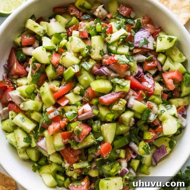Cucumber Salsa in a bowl with tortilla chips, lime wedges, and cilantro on the side.