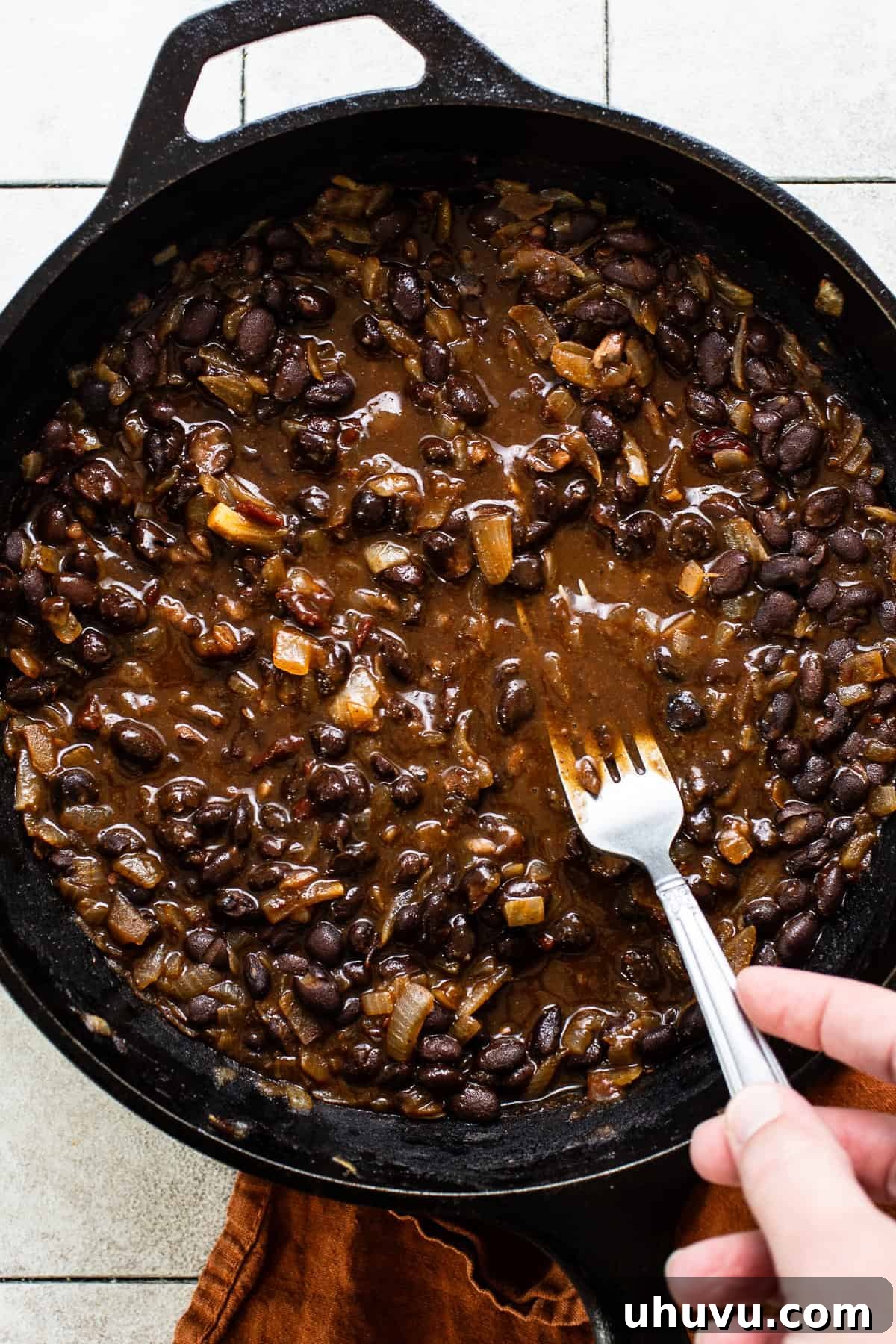 Crispy Black Bean Stacks 6 A fork mashing cooked black beans in a skillet, creating a thick and creamy texture with some chunks for a black bean tostada filling.