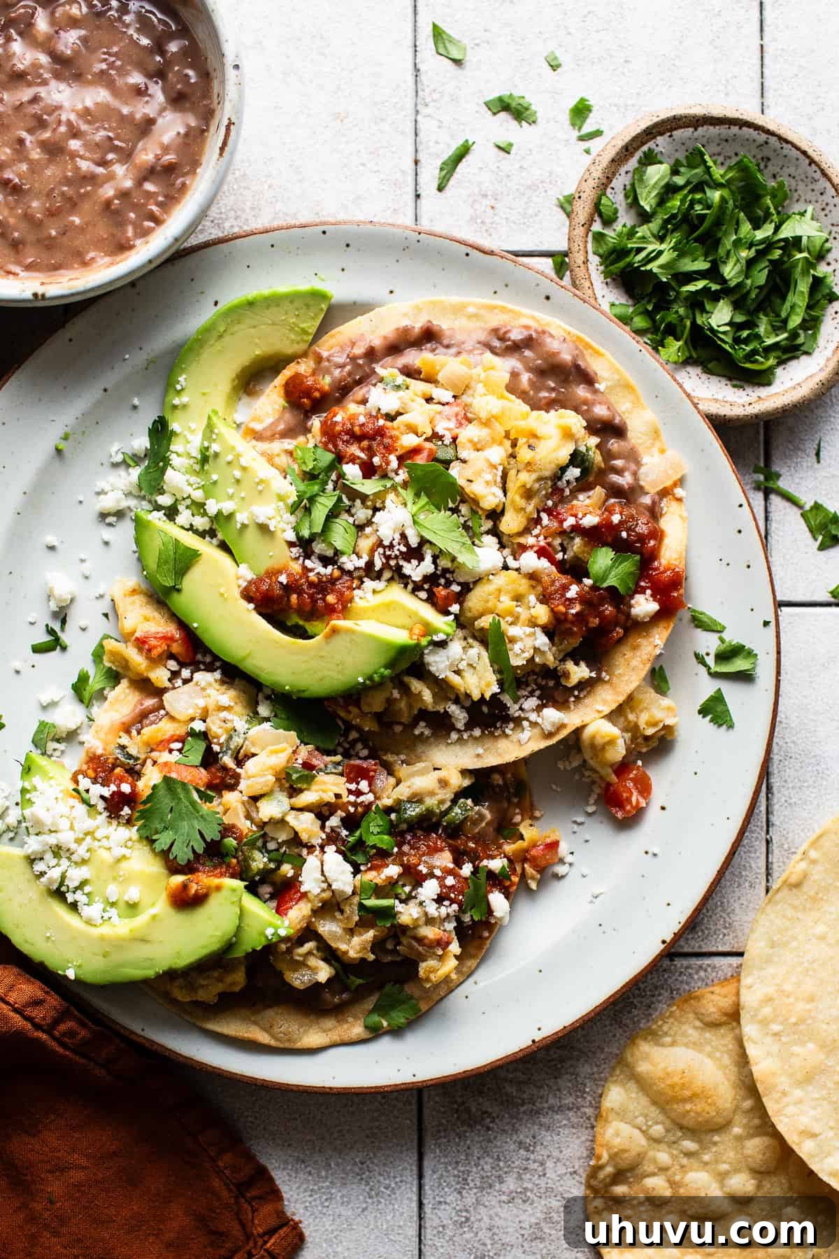 Sunrise Crunch Tostadas 7 A breakfast tostada assembled on a plate with beans, scrambled eggs, salsa, avocado, cotija cheese, and cilantro on top, ready to eat.