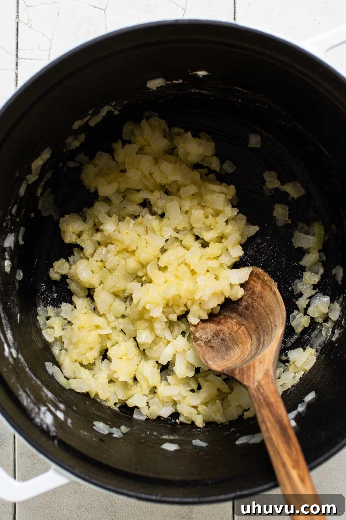 Diced onions and minced garlic being sautéed in a pot with melted butter and olive oil, with cumin added to toast.