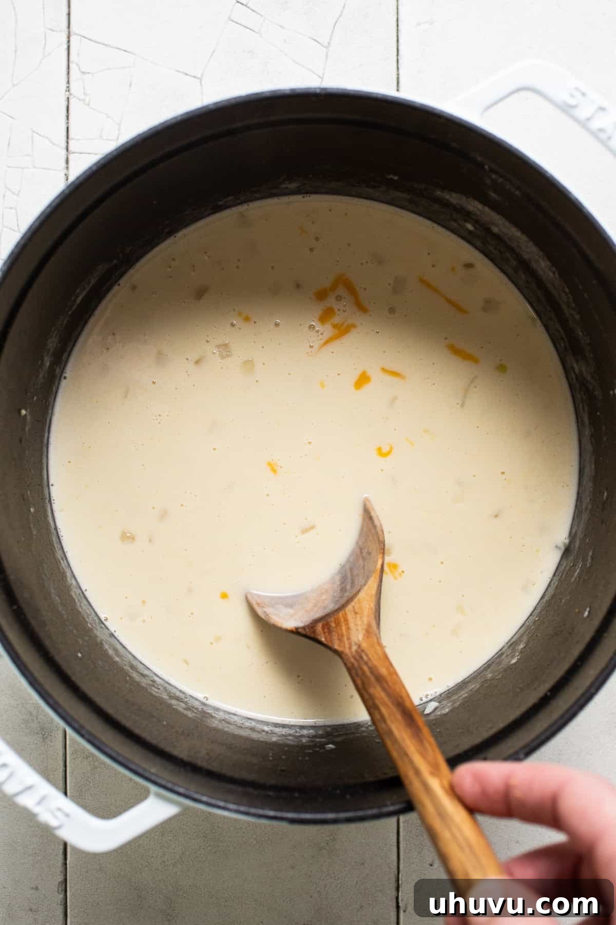 A pot of soup on the stove, with chicken broth, heavy cream, and shredded Monterey Jack and sharp cheddar cheeses being stirred until melted.
