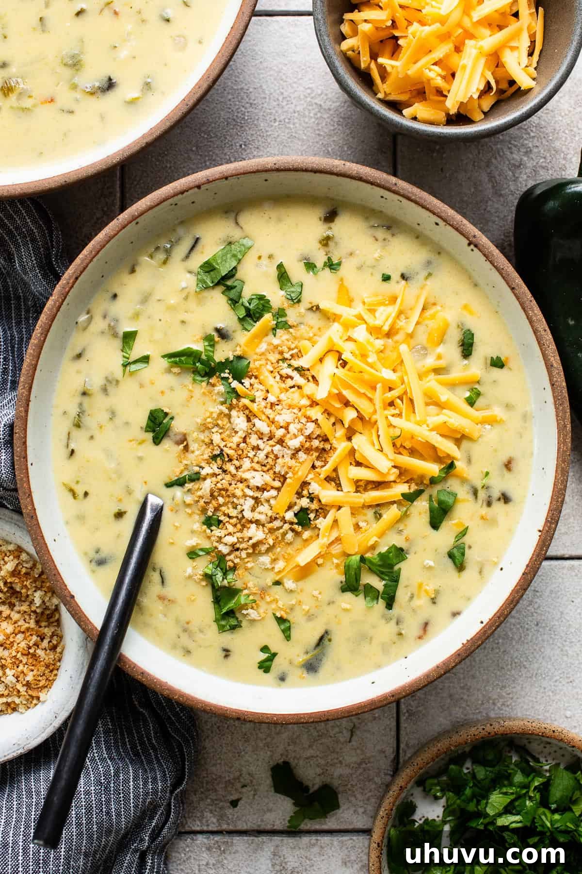 A serving of creamy chile relleno soup in a bowl, garnished with shredded cheese and fresh cilantro, invitingly warm.