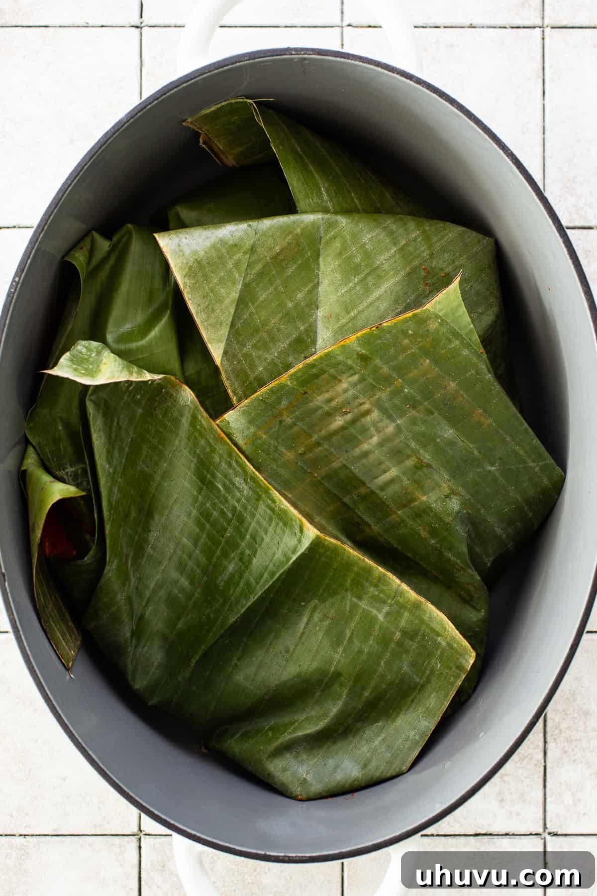 Yucatan's Achiote Slow Roast Pork 6 Marinated cochinita pibil pork wrapped in banana leaves within a large Dutch oven, prepared for slow braising.