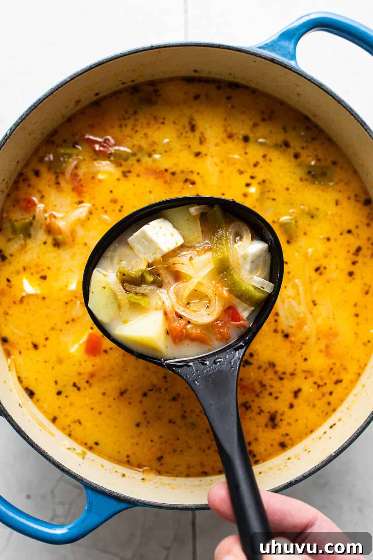 Creamy Cheese Soup 7 A ladle scooping a portion of Caldo de Queso from a large pot, showing the chunky vegetables and cheese.