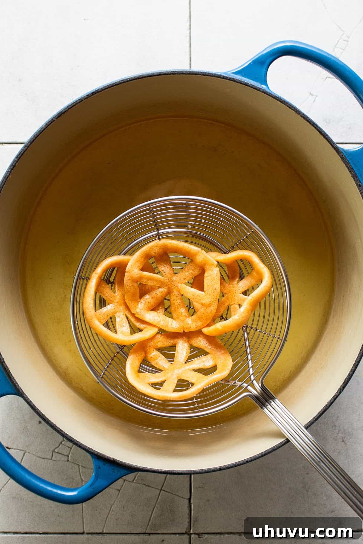 Freshly fried duros being lifted out of oil with a spider strainer, shaking off excess oil.