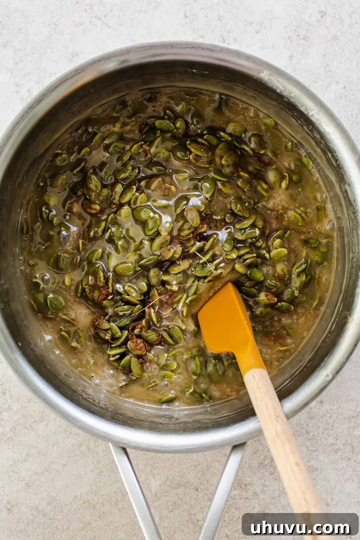Crispy Pumpkin Seed Brittle 5 A saucepan on a stovetop, showing corn syrup, maple syrup, warm spices, and roasted pepitas being mixed together to form the brittle base.