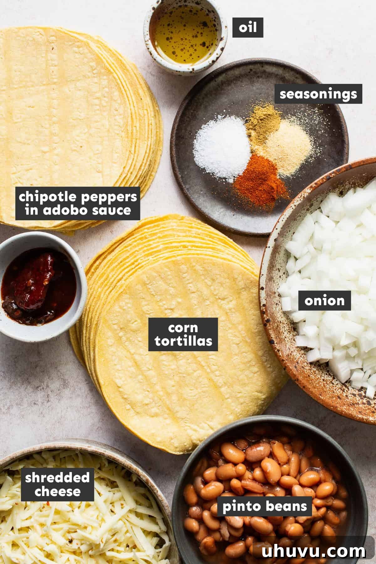 All the fresh ingredients laid out on a wooden table, ready for preparing bean and cheese taquitos, including onions, beans, chipotles, spices, tortillas, and cheese.