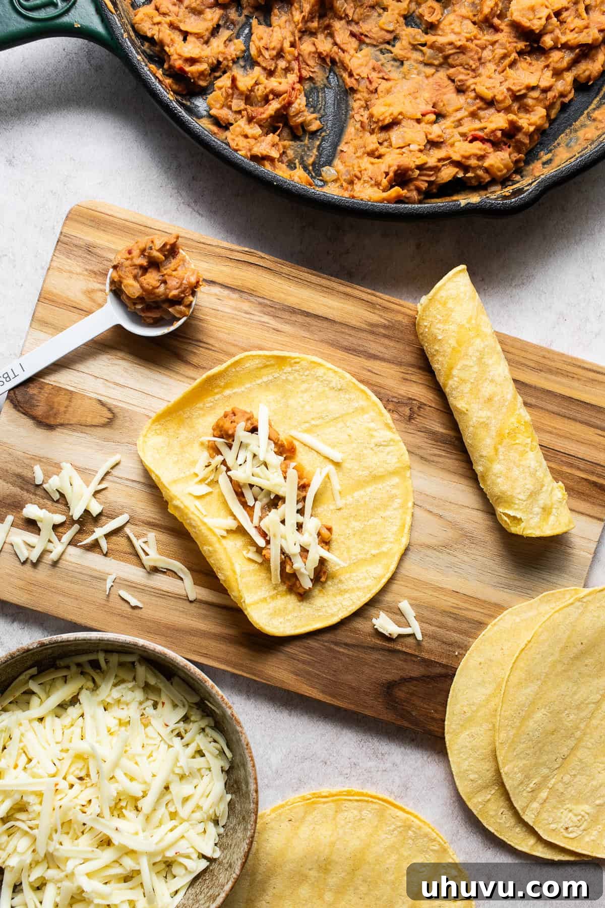A corn tortilla being carefully filled with the bean mixture and shredded cheese, ready to be rolled into a taquito.