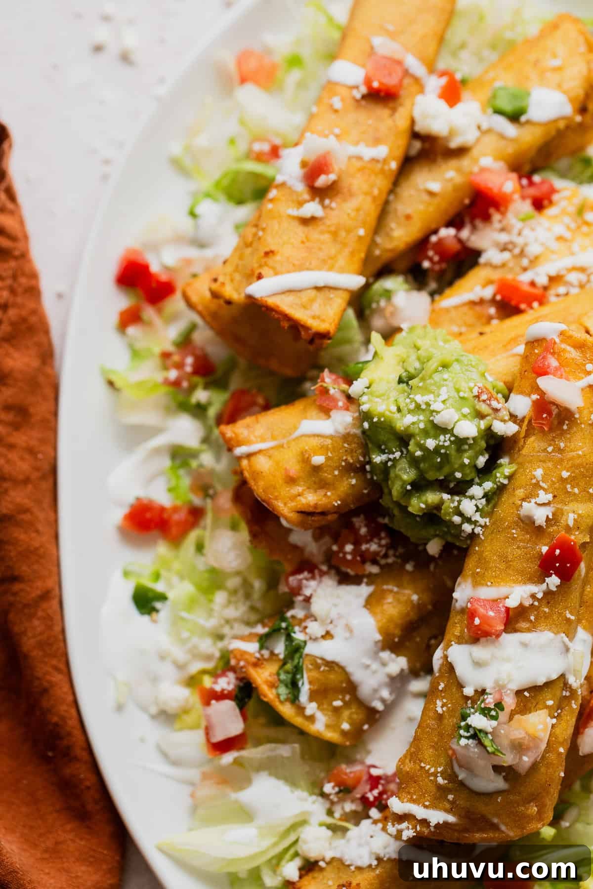 Two crispy taquitos drizzled with creamy Mexican crema and served alongside a dollop of fresh guacamole, ready to be enjoyed.