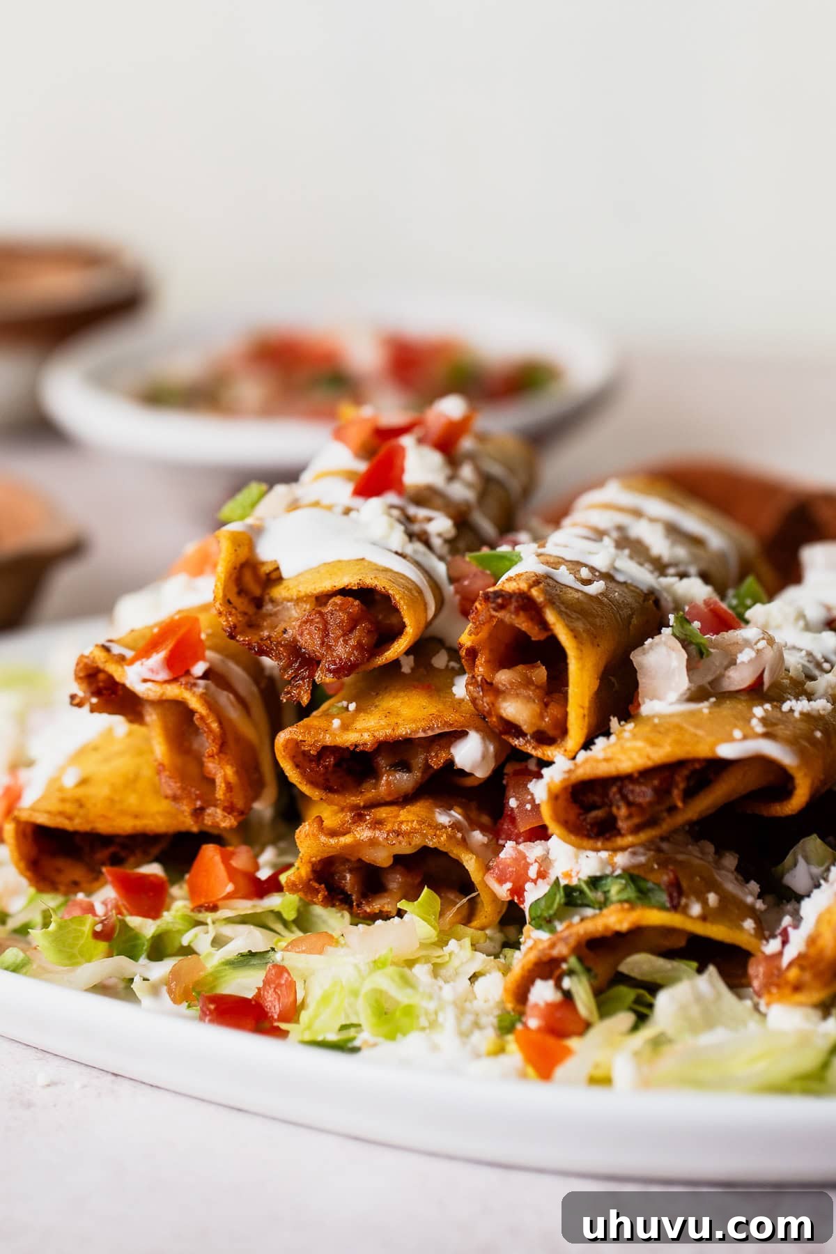 A close-up of crispy bean and cheese taquitos stacked on a plate, showing the golden exterior and a glimpse of the delicious filling.