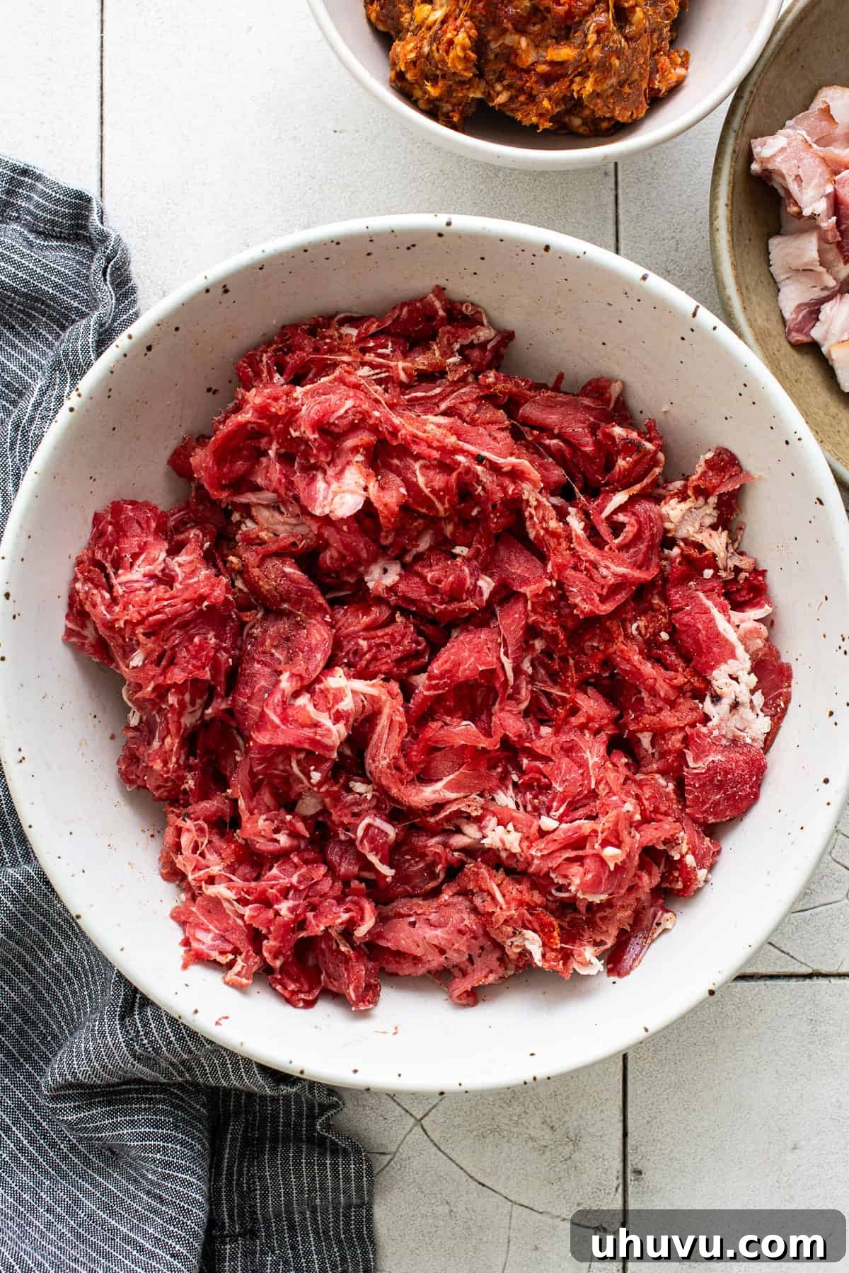 Thinly shaved steak seasoned with a blend of spices in a bowl, ready for cooking.
