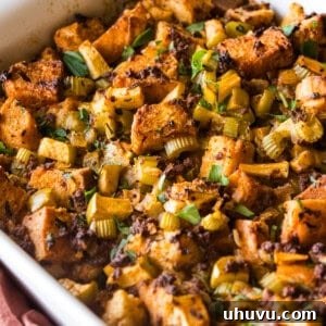A baking dish of chorizo stuffing garnished with fresh parsley and made with apples, onion, and celery.