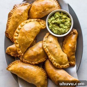 Beef empanadas on a platter with a bowl of guacamole on the side.