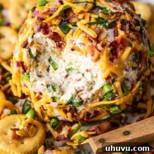 An easy jalapeño cheese ball covered with bacon and cheddar on a plate with crackers.