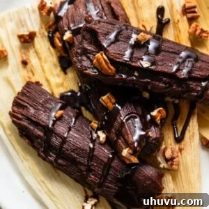Chocolate tamales drizzled with a chocolate sauce and chopped pecans on a corn husk.