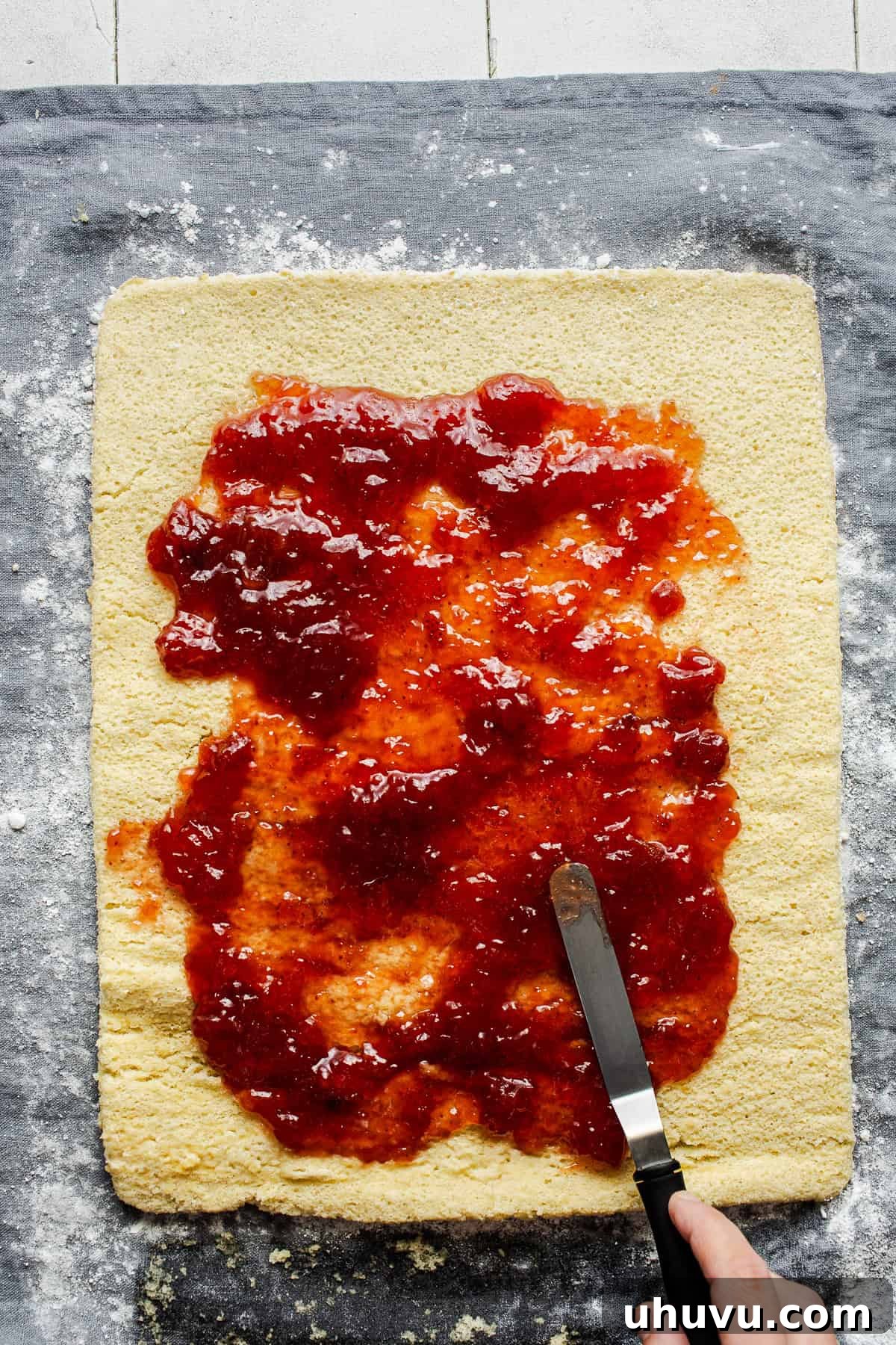 Wrapped Meat Bundles 7 The unrolled sponge cake is generously slathered with bright red strawberry jam, preparing it for its final roll.