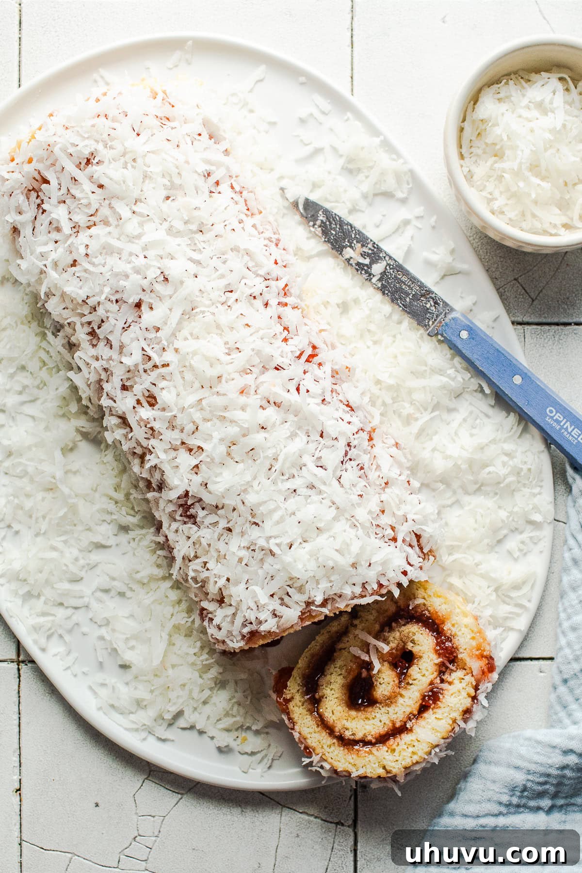 Wrapped Meat Bundles 8 A long, perfectly rolled Niño Envuelto, covered completely with sweet shredded coconut, resting on a white plate, ready to be sliced.