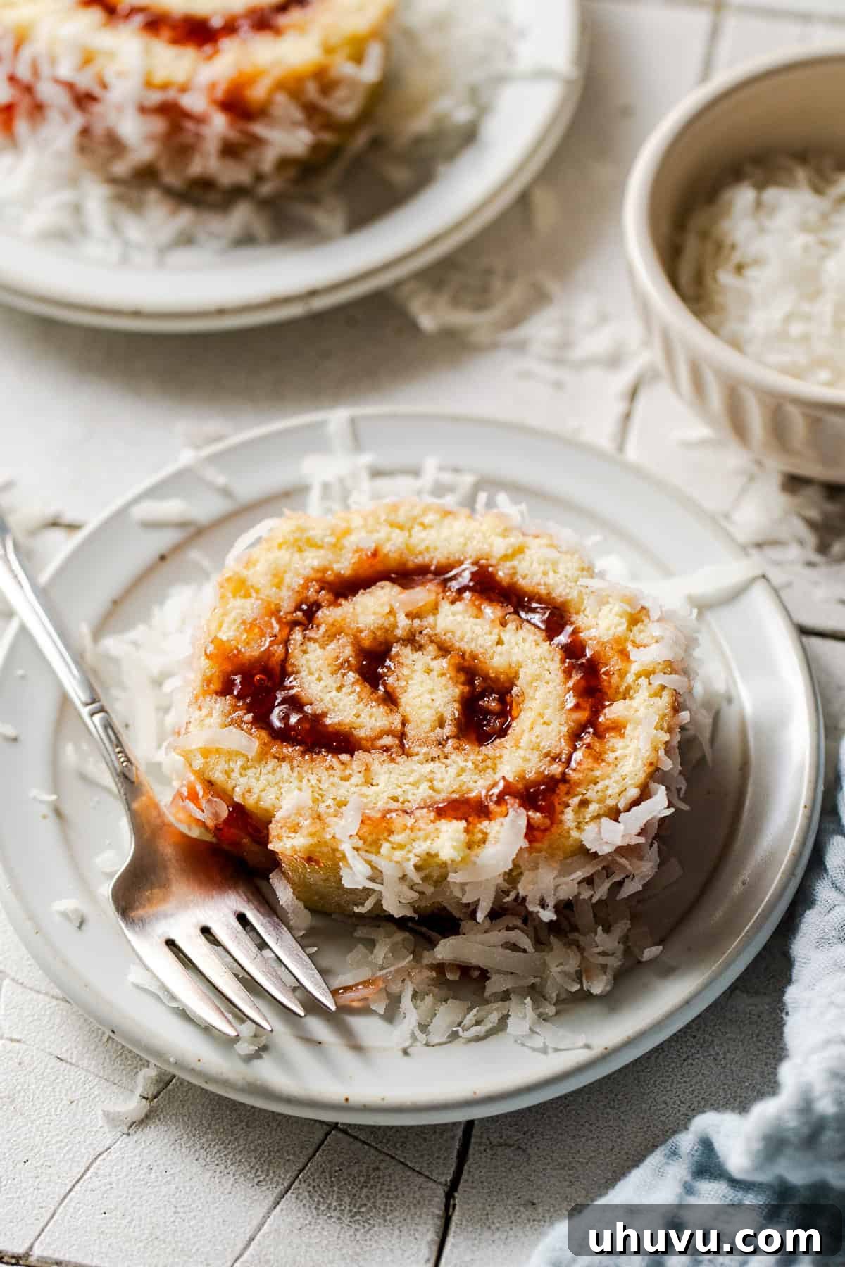 Wrapped Meat Bundles 9 A perfectly sliced piece of Niño Envuelto, showcasing the strawberry jam swirl and coconut coating, served on a white plate with a fork.