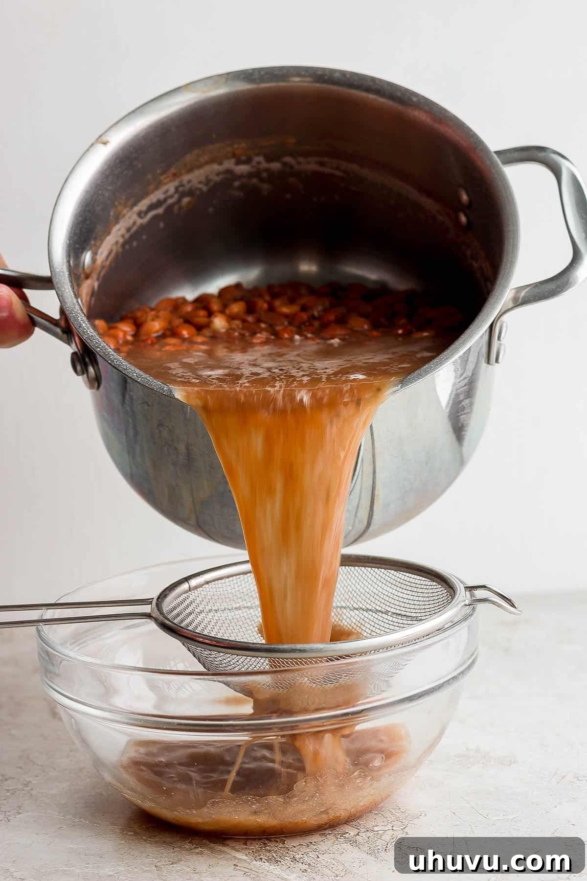 Velvety Frijoles 7 Cooked pinto beans being poured through a colander and into a bowl to save the bean cooking liquid.