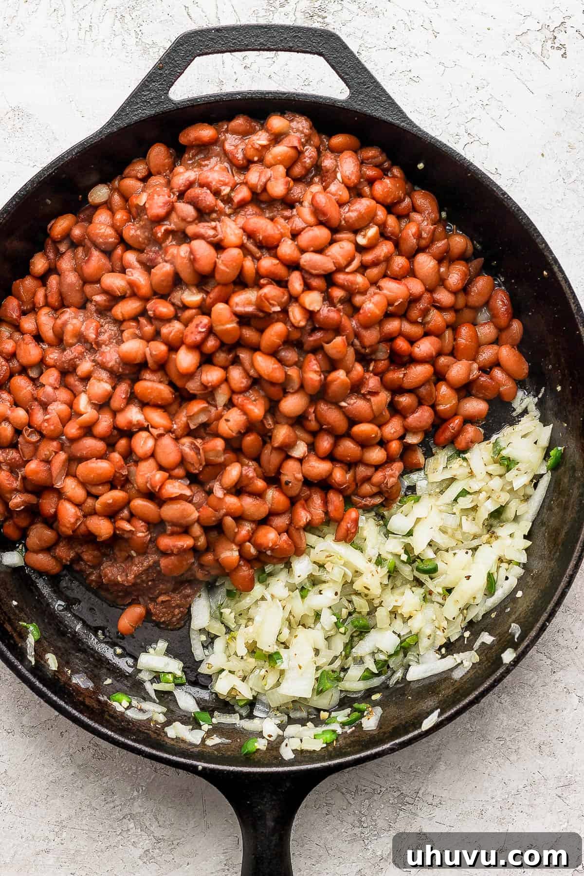 Velvety Frijoles 9 Cooked pinto beans in a skillet with onions, jalapenos, and garlic.